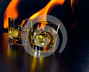 Glasses of whiskey with ice cubes in front of the flame