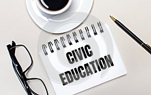 Glasses, a white cup of coffee, a white notebook with the words CIVIC EDUCATION and a ballpoint pen lie on a light background.