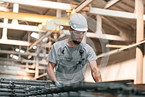 In glasses and white hard hat. Young factory worker in grey uniform