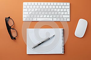 Glasses white mouse keyboard notepad and pen on orange background