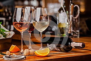Glasses of white, rose and red wine are on the table, a bottle and corks are nearby. Glasses are on the table in the bar