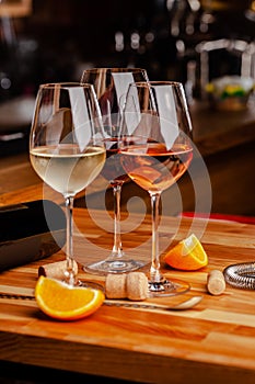 Glasses of white, rose and red wine are on the table, a bottle and corks are nearby. Glasses are on the table in the bar