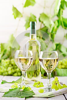 Glasses with white wine, fresh grapes and a bottle of white wine on a wooden table.