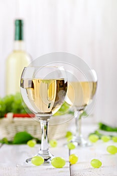 Glasses with white wine, fresh grapes and a bottle of white wine on a wooden table.