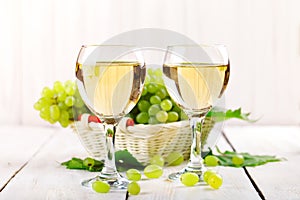 Glasses with white wine and fresh grapes on a wooden table.