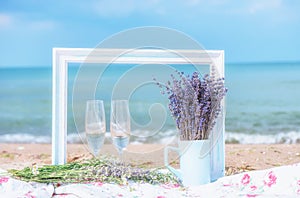 Glasses with white wine and lavender flowers on the pstilka on the beach by the sea. Summer light still life, the atmosphere of re