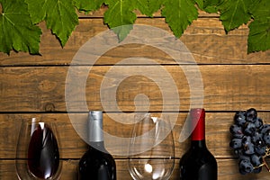 Glasses of wine bottles and grapes and leaves on wooden background. Top view with copy space