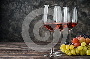 Glasses of wine and grapes on wooden table against grey background