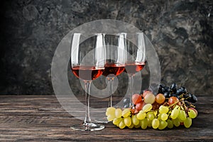 Glasses of wine and grapes on wooden table against grey background