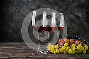 Glasses of wine and grapes on wooden table against grey background