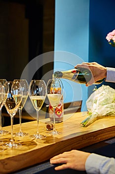 Glasses of wine stand on a wooden bar - waiter`s hands pour champagne into a glass