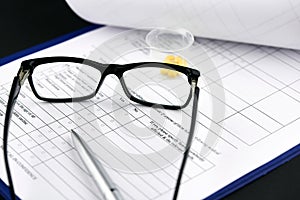 Glasses, yellow pills in graduated glass and pen on medical questionnaire form