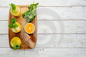 Glassware with refreshing citrus fruits cocktail on white wooden background.