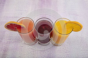 Glassware with refreshing citrus fruits cocktail on white wooden background. Antioxidant juices of Pomegranate Juice, Orange Juice