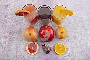Glassware with refreshing citrus fruits cocktail on white wooden background. Antioxidant juices of Pomegranate Juice, Orange Juice