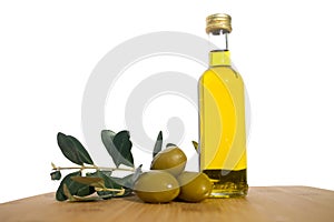 Glassy bottle of olive oil with group of green shiny olives and brunches with leafs