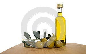 Glassy bottle of olive oil with group of green shiny olives and brunches with leafs