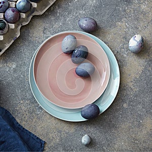 Glazed ceramic plate in a color of Living Coral Pantone with painted violet Easter eggs on a gray stone background, copy