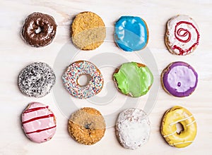 Glazed colorful doughnuts with sprinkles and icing on white wooden background, top view