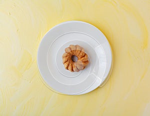 Glazed cruller on a plate atop a yellow background