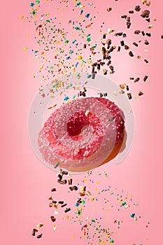 Glazed donut levitates with sprinkles on a pink background
