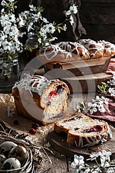 Glazed Easter cake or bread kulich with cherry on rustic wooden table with easter eggs in nest and spring flowers. Happy Easter