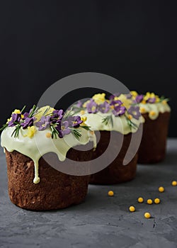 Glazed easter cake decorated with purple flowers and candies on dark background, copy space. Happy Easter holidays. Kulich