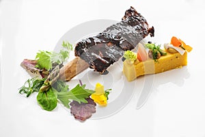 Glazed short rib with polenta, bean cream, vegetables and wild herb salad on a white plate, meat dish as main course in a gourmet