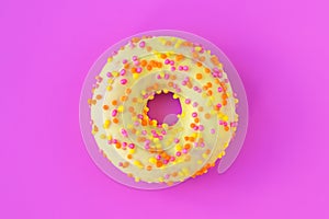 Glazed yellow donut with multicolored sprinkles on bright pink background. Unhealthy high-calorie food. Fun mood concept. Laconic photo