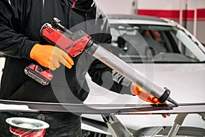 Glazier applying rubber sealing to windshield in garage, close up.