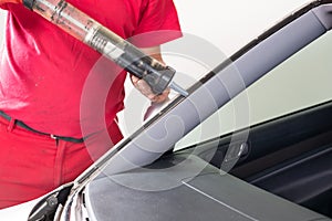 Glazier using application gun to apply adhesive for windscreen