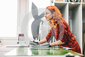 Glazier woman worker cutting glass in workshop.