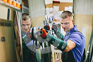 Glazier worker holding a big mirror glass pane in workshop.