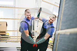 Glazier worker holding a big mirror glass pane in workshop.