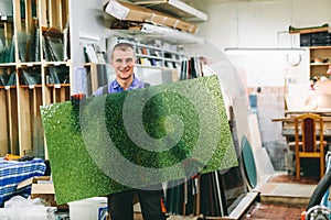 Glazier worker holding a green glass pane in workshop.