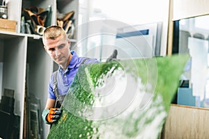 Glazier worker holding a green glass pane in workshop.