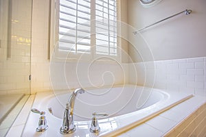 Gleaming built in bathtub and window with blinds inside a bathroom