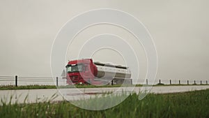 A gleaming semitrailer tank truck transports liquid cargo in bad rainy weather. Copy space for text. Slow motion