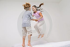 Gleeful giggles. two little children jumping on a bed together.