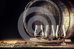 Glencairn whiskey tasting cups on a wooden serving, with a whisky barrel in the dark background