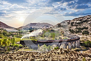 Glenfinnan Railway Viaduct in Scotland with the Jacobite steam train against sunset over lake