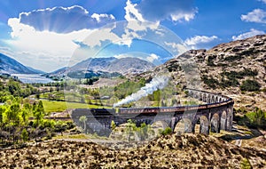 Glenfinnan Railway Viaduct in Scotland with the Jacobite steam train against sunset over lake