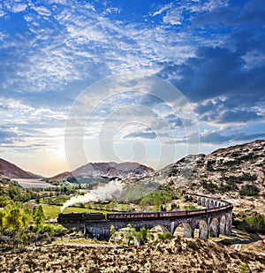 Glenfinnan Railway Viaduct in Scotland with the Jacobite steam train against sunset over lake