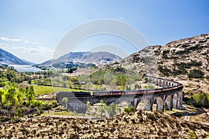 Glenfinnan Railway Viaduct in Scotland with the Jacobite steam train against sunset over lake