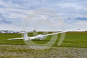 Glider plane standing on grass airport runway with dramatic sky background