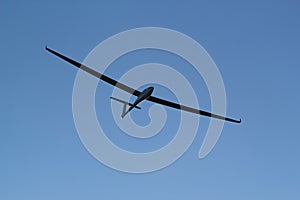 Glider silhouette flying against the blue sky with clouds and sunlight