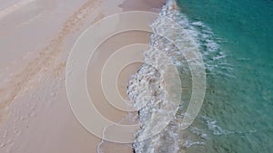 Gliding aerial view above sandy beach with waves