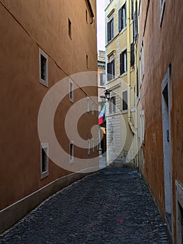 A glimpse of a narrow empty Roman street, Vicolo del Monticello with the Italian flag in the background, Rome, Italy