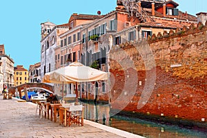 Glimpse of Venice with one of its canals with boats, historic buildings and people drink and relax in outdoor table and chairs of