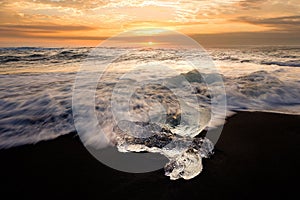 Glistening chunk of ice sits in the sand on a beach, illuminated by the glimmer of the sun